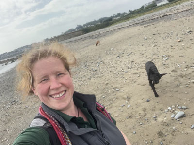 Jenny at the beach with dogs running in the background.