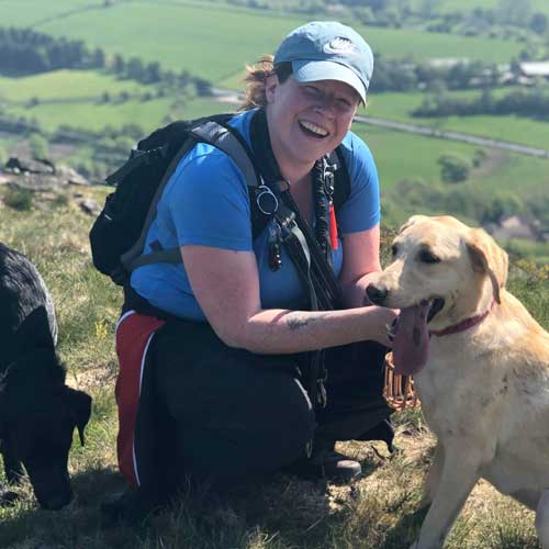 Jenny wearing walking equipment, crouched with a labrador.